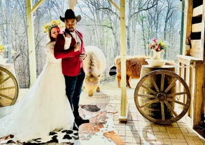 A bride hugs her husband under the western barn themed arbor at a small intimate barn wedding venue in Lynchburg. Cows stand behind grazing.